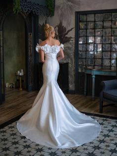 a woman in a white wedding dress is looking at something on the wall behind her