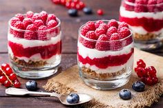 three desserts with raspberries and yogurt are on a wooden table