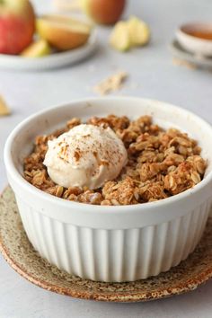 a white bowl filled with granola and topped with vanilla ice cream next to apples