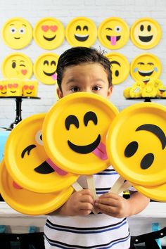 a young boy holding up yellow plates with smiley faces on them