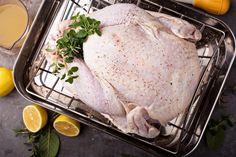 a whole chicken sitting on top of a metal pan next to lemons and herbs