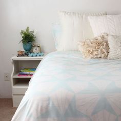 a bed with white and blue comforters, pillows and a book shelf in the corner