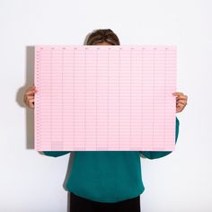 a woman holding up a pink piece of paper with numbers and lines on it in front of her face