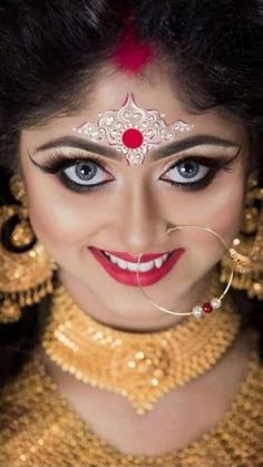 a woman with blue eyes and gold jewelry on her face is smiling at the camera