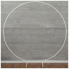 a white metal circle on a stand against a gray wall with wood flooring in the background