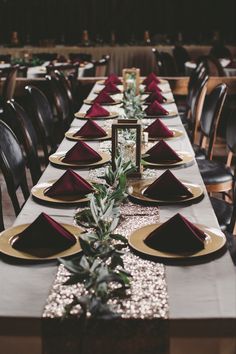 a long table set with place settings and gold chargers on it, along with red napkins