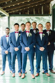 a group of men standing next to each other wearing suits and bow ties in front of a building