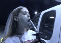 a woman with her mouth open is drinking from a blow dryer in front of a white truck