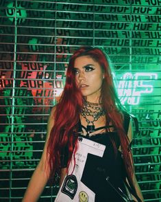 a woman with long red hair standing in front of a green and black background wearing punk clothing