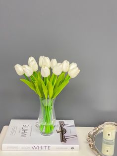 white tulips in a glass vase on top of a book next to a candle