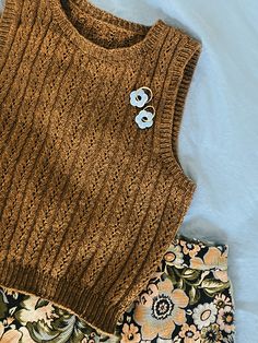 a brown sweater and floral shorts on a white bed with a blue flowered pillow