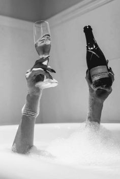 two people are in the bathtub holding up wine bottles and champagne glasses to each other