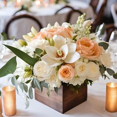 a vase filled with white and peach flowers on top of a table next to candles