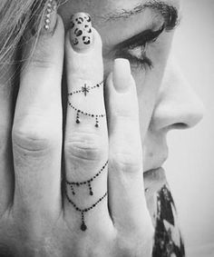 a woman holding her hand up to her face with a cross tattoo on the middle finger