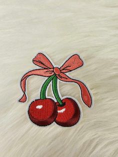 a pair of cherries with a pink bow on a white fur background, embroidered onto the back of a jacket