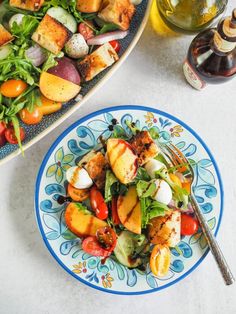 a salad with chicken, tomatoes and other vegetables on a blue and white plate next to a glass of wine