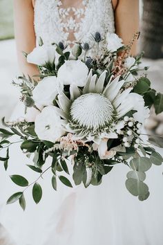 a bride holding a bouquet of white flowers and greenery