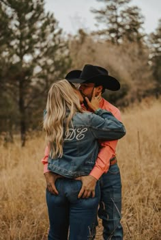 a man in a cowboy hat hugging a woman on the cheek while standing in tall grass