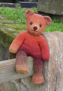 a knitted teddy bear sitting on top of a wooden bench