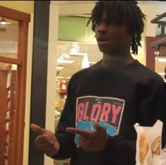 a man standing in front of a store holding a hot dog and pointing at something