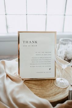 a thank card sitting on top of a wooden table next to a glass of wine