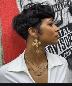 a woman standing in front of a graffiti wall wearing earrings and a white shirt with gold cross pendants on her neck