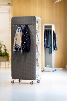 a rack with clothes and sweaters hanging on it in a room next to a plant