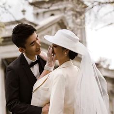 a man and woman dressed in wedding attire standing next to each other, one wearing a white hat