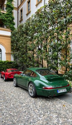 two green sports cars parked next to each other on a cobblestone street in front of an apartment building