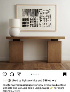 a white vase sitting on top of a wooden table next to a framed art piece