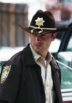 a man wearing a sheriff hat while standing in front of a car on the street