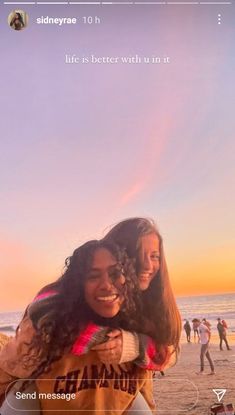 two young women hugging each other on the beach with people in the background and an orange sky