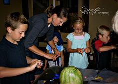 a group of children standing around a table with watermelon slices on top of it