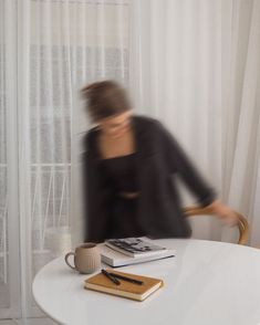 a blurry image of a person sitting at a table with books and a cup