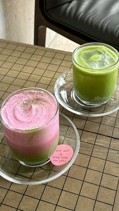 two drinks are sitting on the table next to each other, one is green and pink