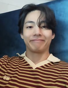 a young man with black hair wearing a brown and white striped shirt smiling at the camera