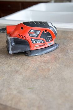 a red and black cordless sander sitting on top of a counter