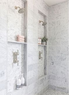 a bathroom with white marble walls and shelves on the wall, along with two shower heads