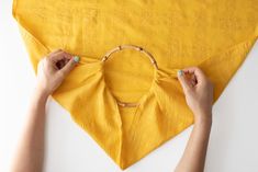 two hands holding up a piece of yellow fabric to the top of a triangle shaped object