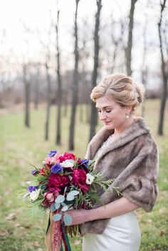 a woman in a fur coat holding a bouquet with red, purple and blue flowers