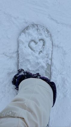 someone is standing in the snow with their feet up and there is a heart drawn on the snowboard