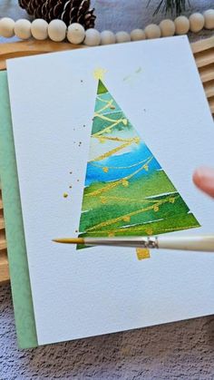 someone is painting a christmas tree with watercolors on the paper and using a brush