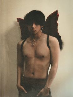 a shirtless man with wings on his head standing in front of a white wall