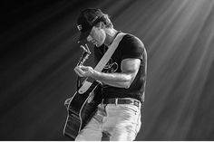 a man holding a guitar while standing on top of a stage in front of light beams