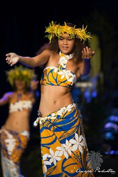 a woman in a yellow and blue dress dancing on stage with other dancers behind her