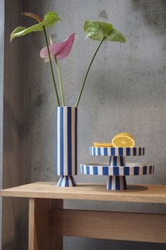 two flowers are in a striped vase on a table next to a slice of lemon