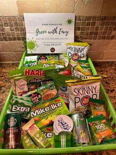 a green tray filled with lots of different types of snacks and drinks next to a sign