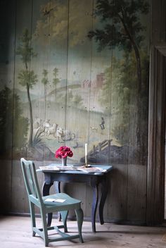 a small table and chair in front of a wall with a painting on the wall