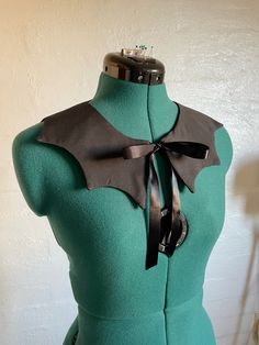 the back of a green dress with a black bow tie on it's neck