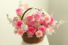 a basket filled with pink and white flowers on top of a table next to a wall